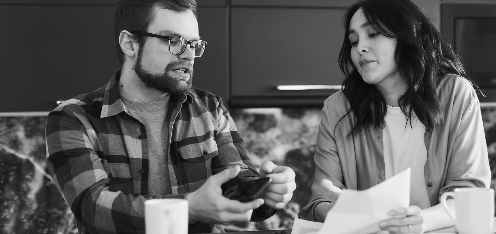 Man and woman holding paper and smart phone at kitchen table