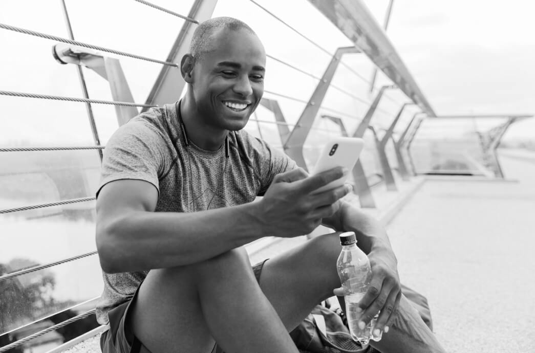 Man smiling after working on while holding bottled water and looking at his smart phone