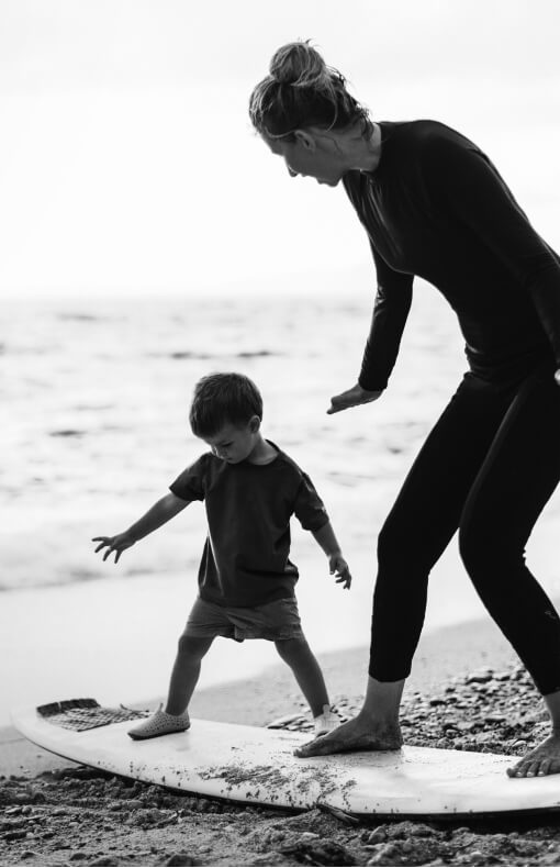Mother and young son at the beach practicing standing on a surf board