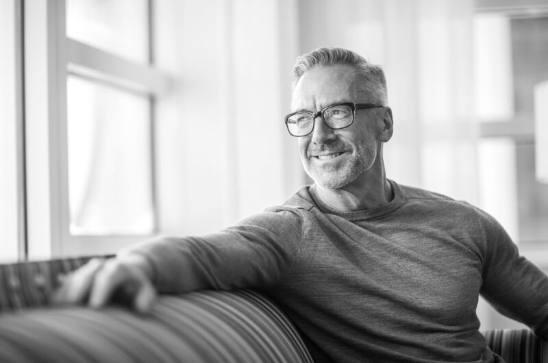 Mature man smiling on couch while looking out a window