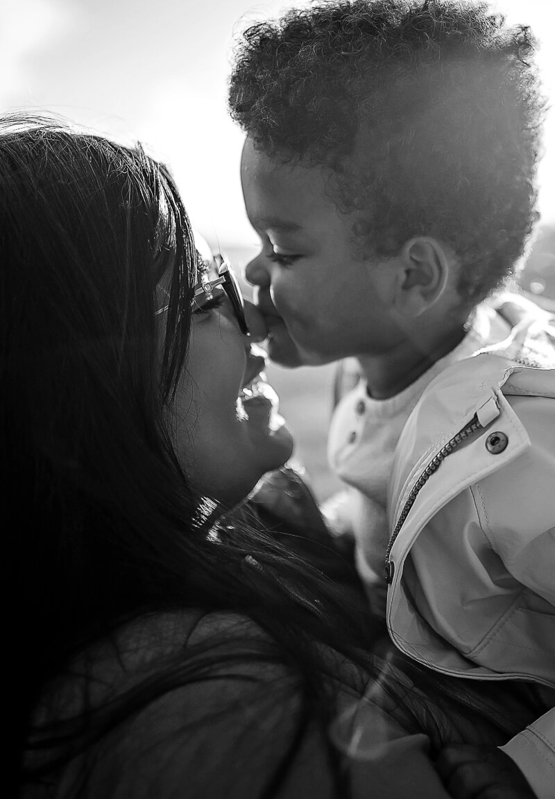 Mother smiling while holding son outside as son kisses her nose