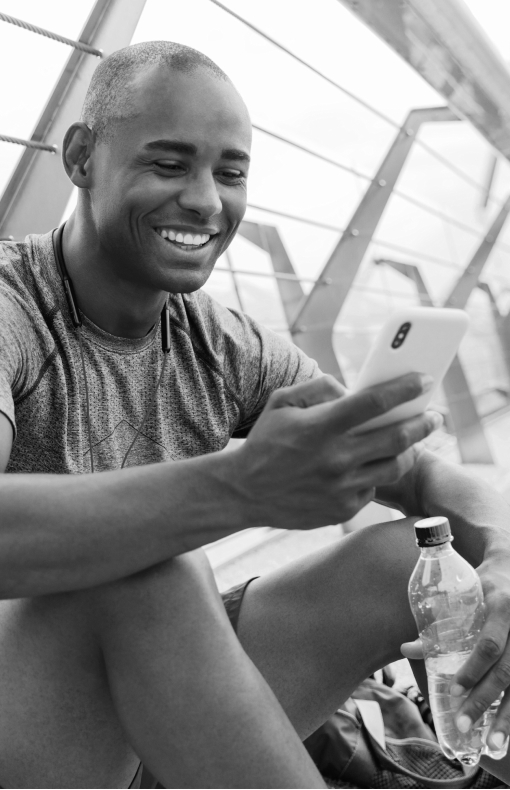 Man smiling after working on while holding bottled water and looking at his smart phone