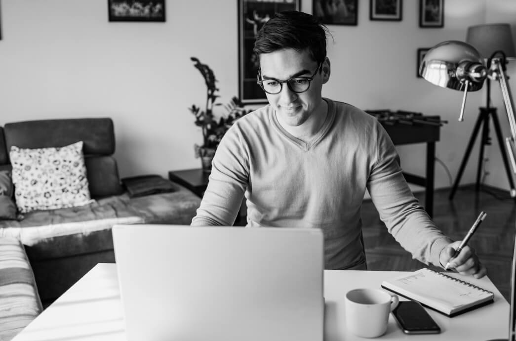 Man seated at home desk working on his laptop and writing in his planner